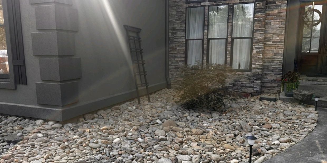 A modern hom with a stone facade, a dry river rock bed, and soft landscaping accents. 