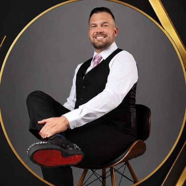 Man in a suit sitting on a chair, smiling.
