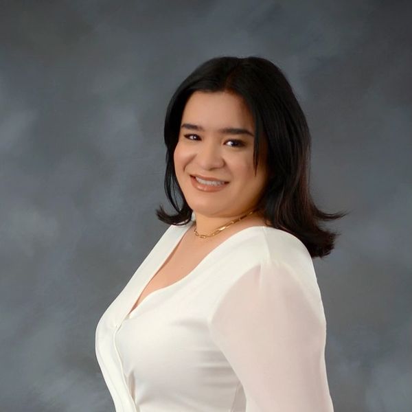 Smiling woman posing in white blouse against gray backdrop.