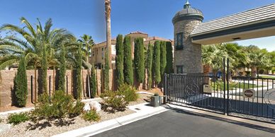 Gated community entrance with palm trees and tall bushes.
