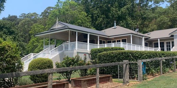 Large white house with a wrap-around porch in a lush green setting.