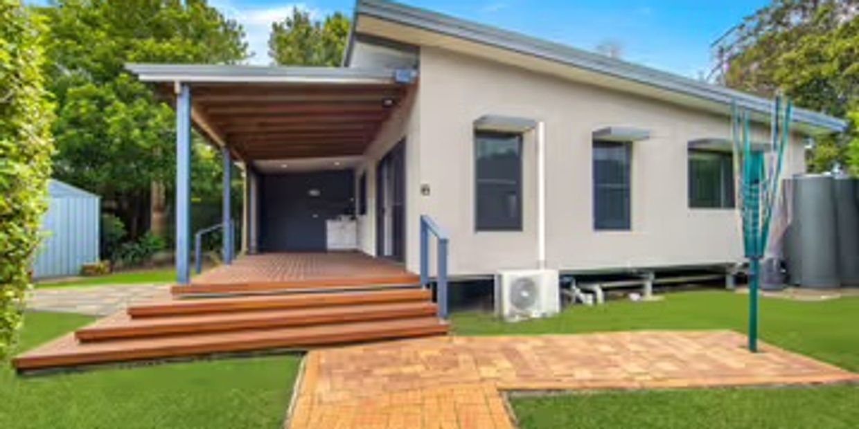 Modern single-story house with wooden deck and green lawn.