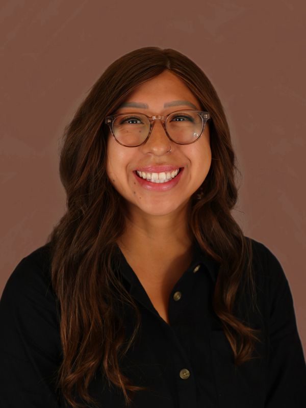 Smiling woman with glasses and long brown hair against a brown background.