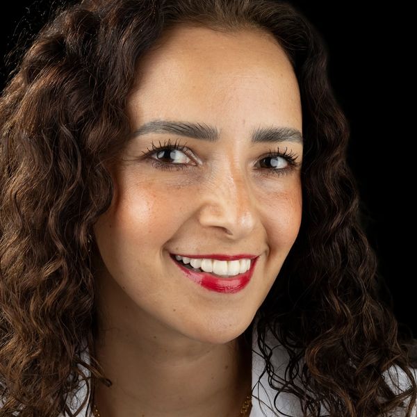 Close-up of a smiling woman with curly hair and red lipstick.