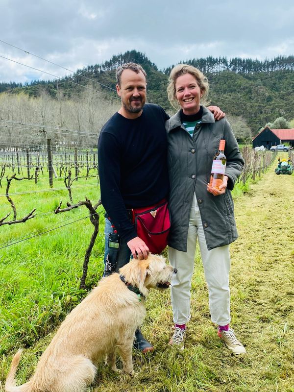 Couple with dog in vineyard holding a wine bottle.