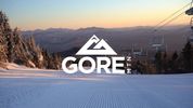 GORE MOUNTAIN LOGO OVER A DOWN MOUNTAIN VIEW WITH SNOW ON THE SLOPE, MOUNTAINS, AND HORIZON DUSK SKY