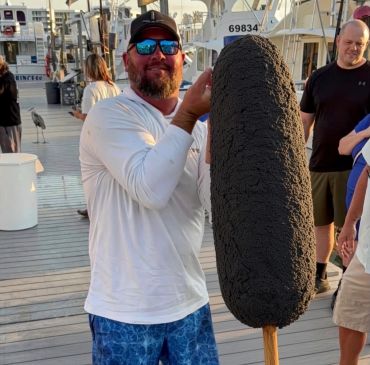 Man holding large, dark, textured object on a dock.