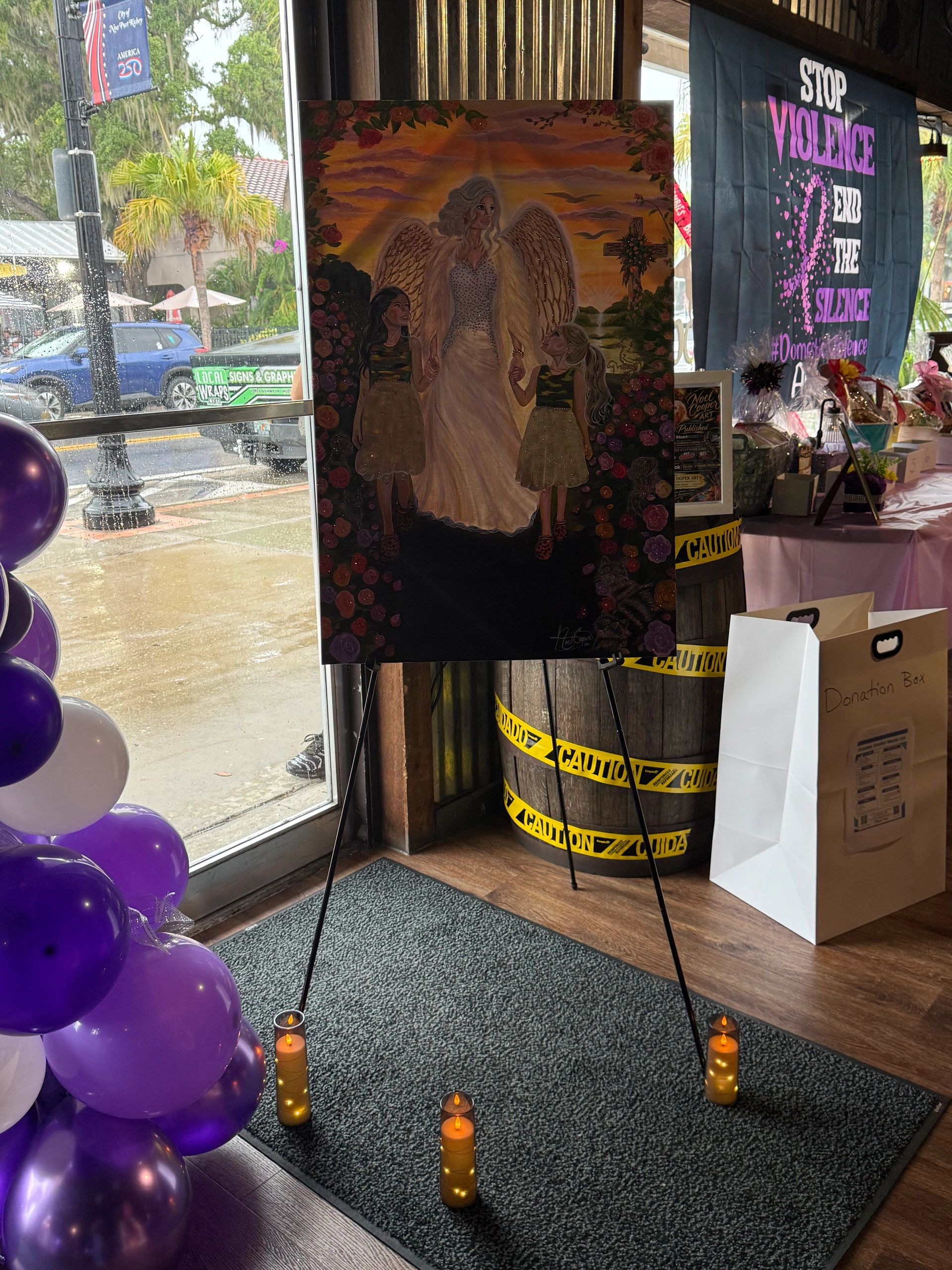 Painting of an angel with two girls, surrounded by candles and a banner against violence.