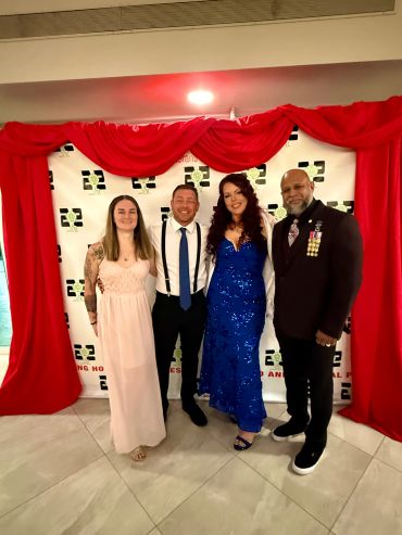 Four people dressed up standing in front of a red curtain backdrop.