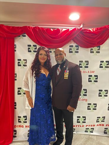 A couple dressed elegantly at an event with a red backdrop.