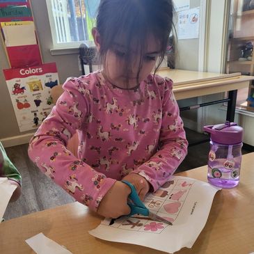 A young girl cutting paper in a classroom.