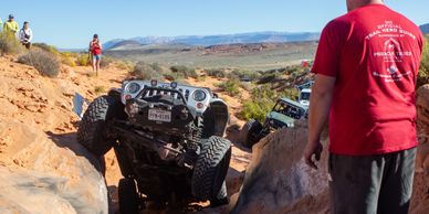 Off-road vehicles navigate rocky terrain with spectators watching.