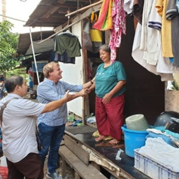 Two men greet a smiling woman outside her home.