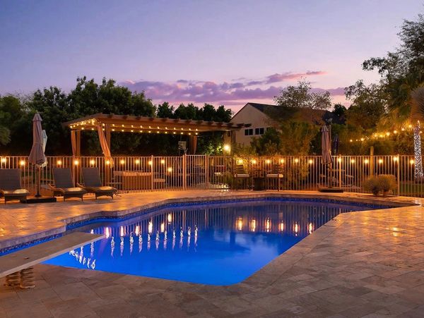 A serene backyard pool with lights, pergola, and chairs at dusk