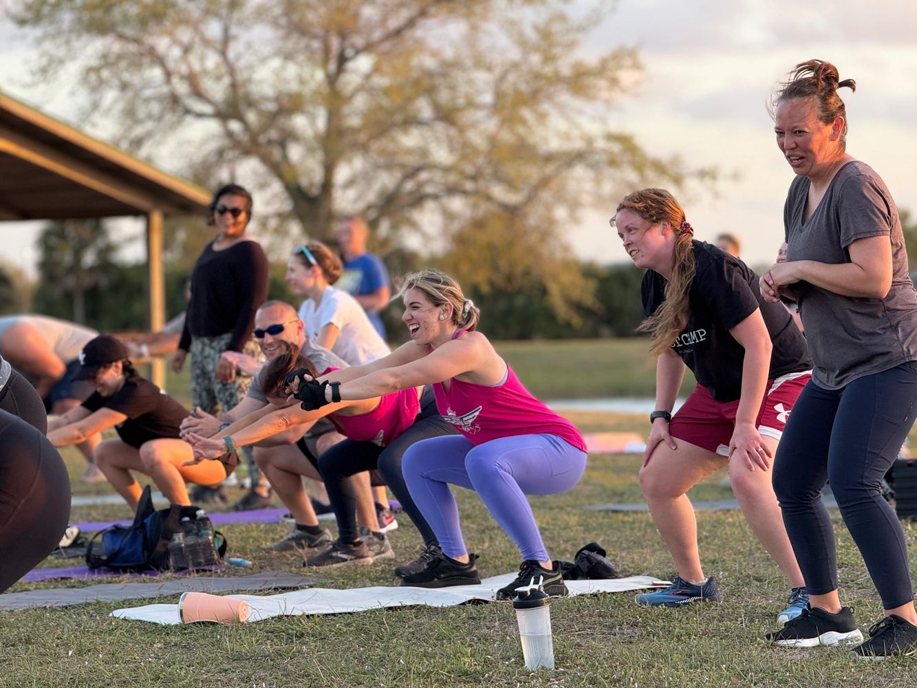 Group of people exercising outdoors, doing squats and lunges on mats.