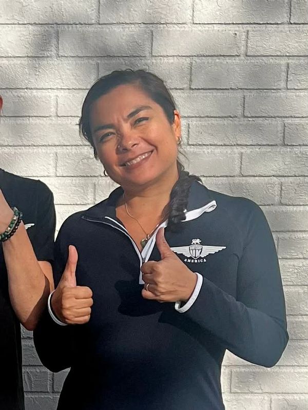Woman smiling and giving two thumbs up in front of a white brick wall.