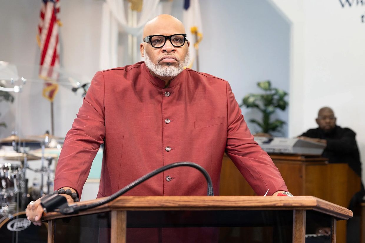 Man in red jacket speaking at a podium in a church setting.