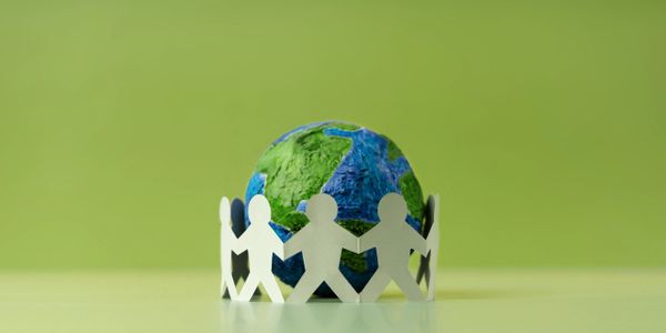 Paper cutout people holding hands around a small globe.