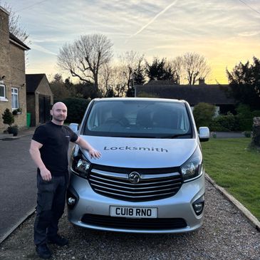 A man stands beside a locksmith van at sunset.