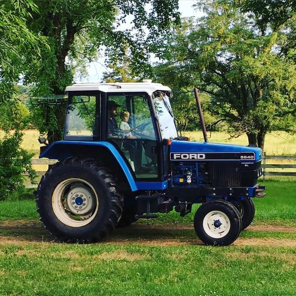 Blue Ford tractor with two people inside on a farm.
