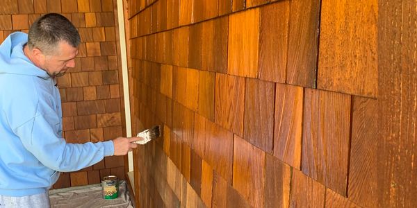 Man staining wooden shingles on a wall.