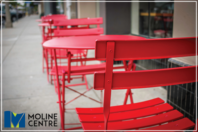 Red bistro tables and chairs as a storefront sidewalk cafe, with the Moline Centre logo