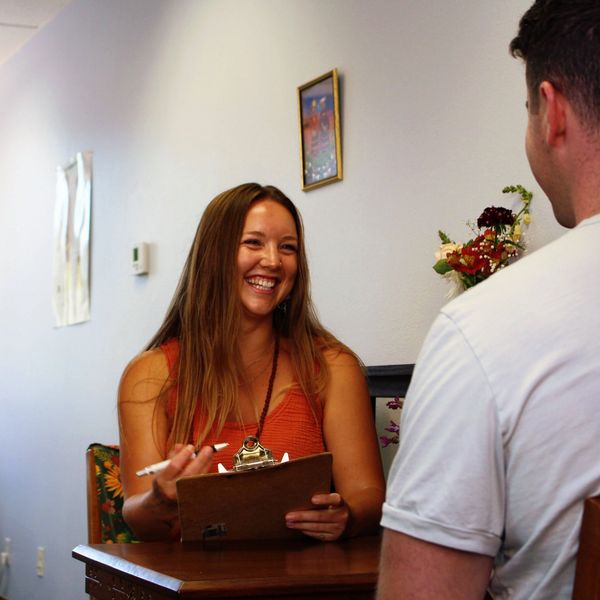 A woman with a clipboard smiles while talking to a man in a white shirt.