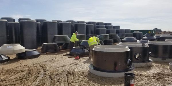 Workers in yellow jackets handling large black industrial pipes outdoors.