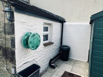 Cozy outdoor corner with stone walls, a green hose reel, and trash bins.