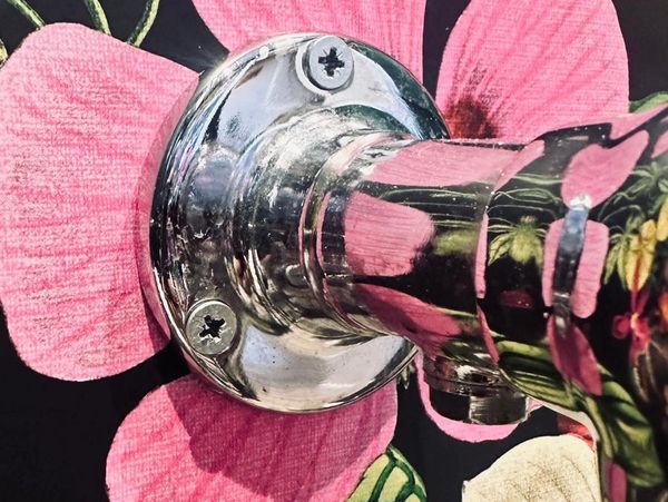 Shiny metal pipe against floral wallpaper with pink and white flowers.