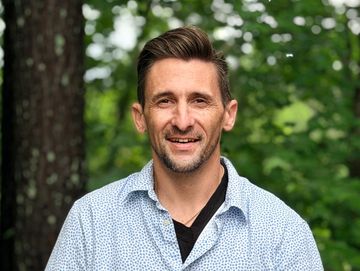 Smiling man outdoors with trees in background.