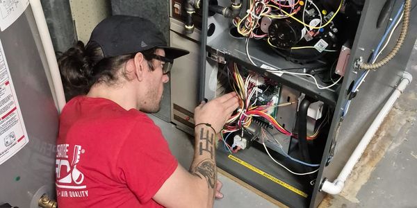 Technician lying on the floor repairing a furnace with exposed wires.