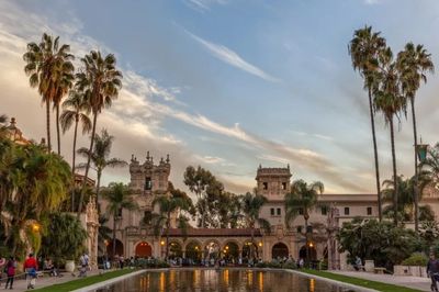 Historic building with palm trees and reflecting pool at sunset.