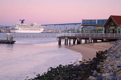 Cruise ship docks near a pier at sunset with a city bridge in the background.