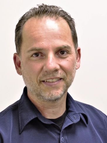Portrait of a smiling man in a dark blue shirt against a plain background.