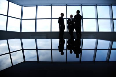 Three businesspeople silhouetted against large windows in a modern office space.