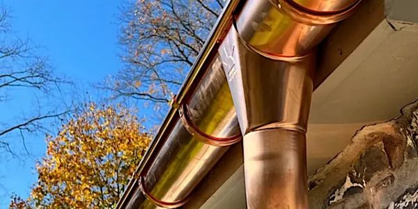 Shiny copper gutter system installed on a house against a clear blue sky.