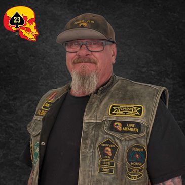 Man with a beard wearing a veteran-themed vest and cap.