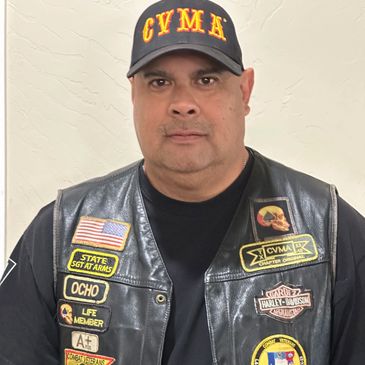 Man wearing a leather vest and cap with military and biker patches.