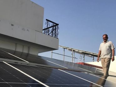 Man standing on a rooftop with solar panels under clear blue sky.