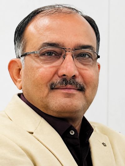 Portrait of a man in glasses and beige blazer.