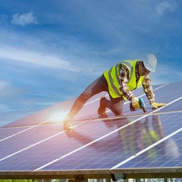 Worker installing solar panels under a blue sky.