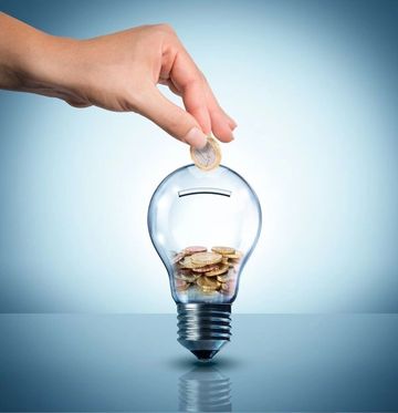 Hand placing coin into a lightbulb-shaped piggy bank.