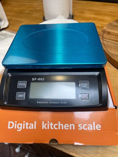 Blue digital kitchen scale on its orange box on a wooden table.