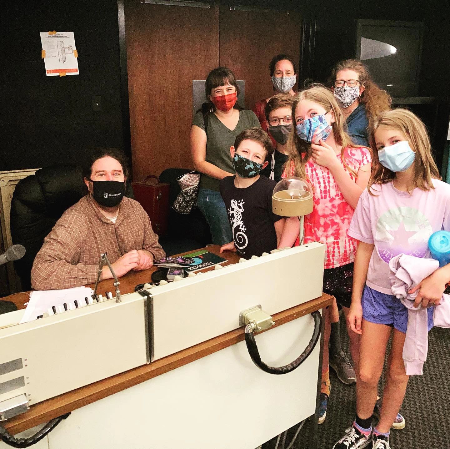 Group of masked people gathered indoors around a desk.
