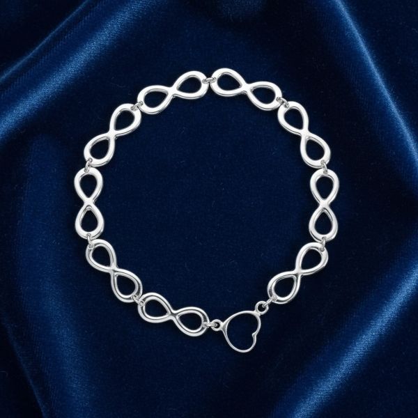 Silver infinity symbol bracelet with a heart-shaped clasp on blue velvet.