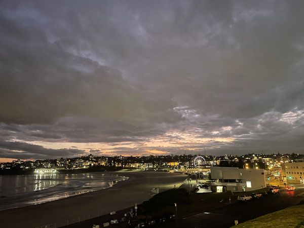 Night view of a coastal town with cloudy sky and illuminated buildings.