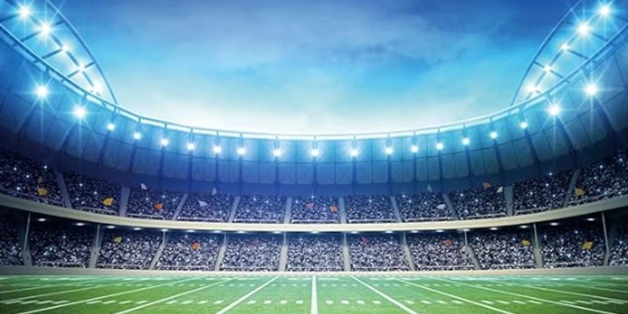 A brightly lit, packed stadium with a green football field under a blue sky.