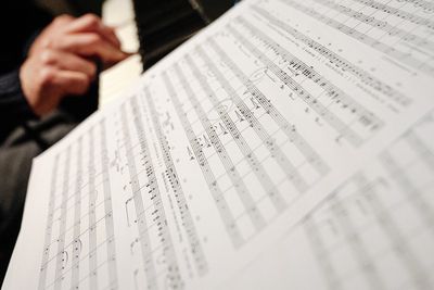 Close-up of sheet music with a hand poised to play piano keys.