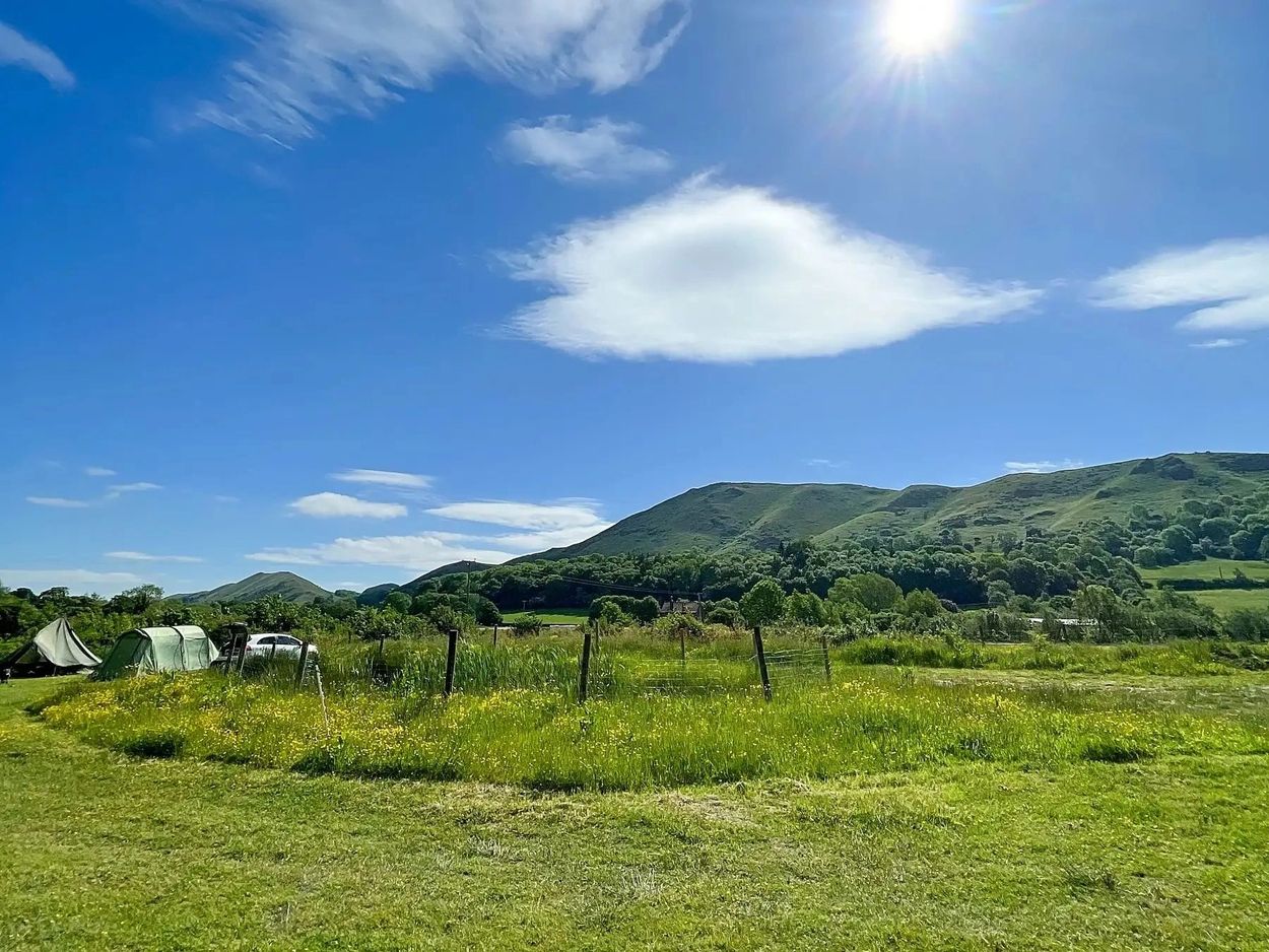 Sunny day at a green campsite with tents and hills.